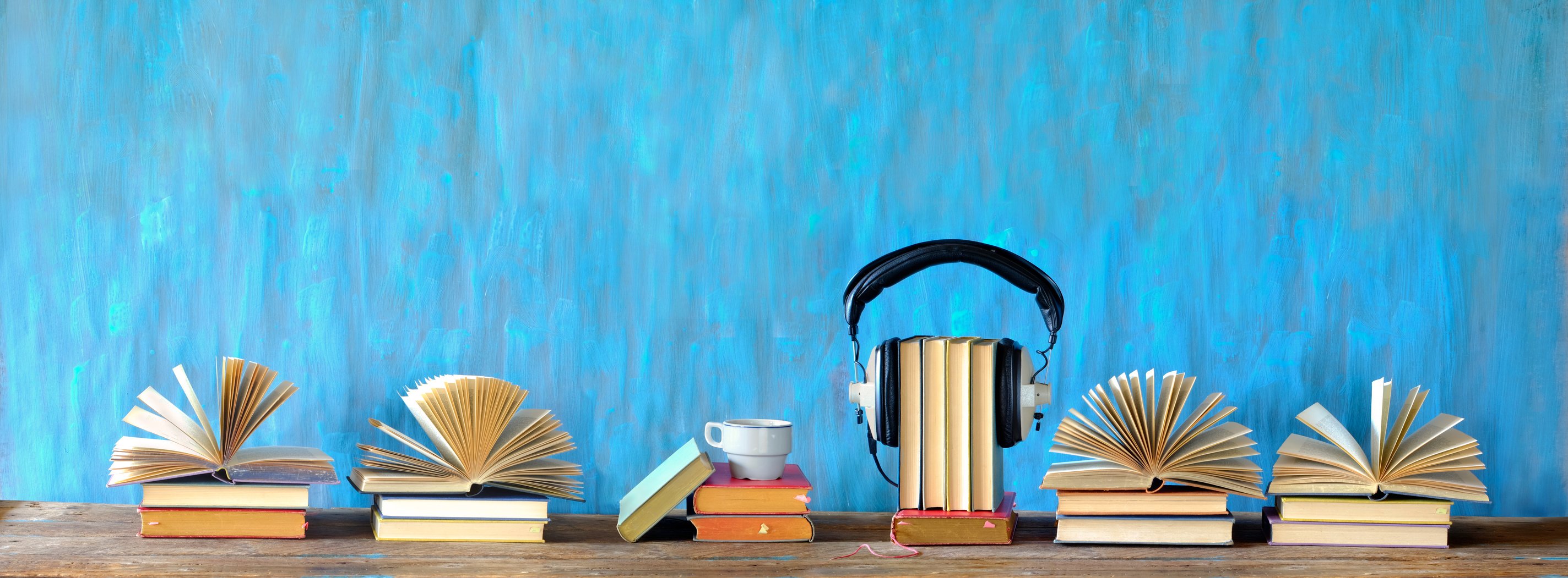 audio book concept with open books, cup of coffee, and vintage headphones, panoramic, good copy space